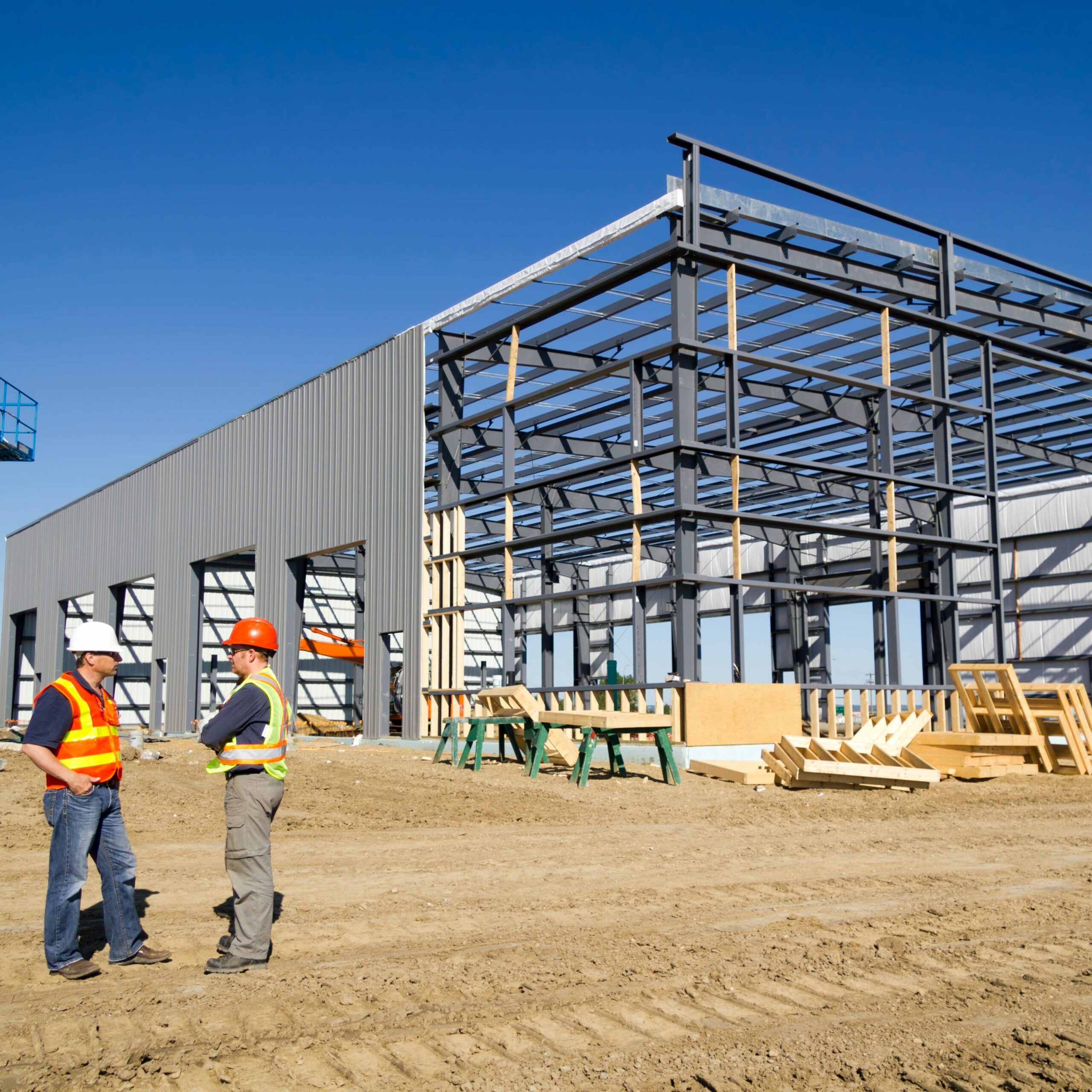 two architects at a construction site, steel building in background under construction.